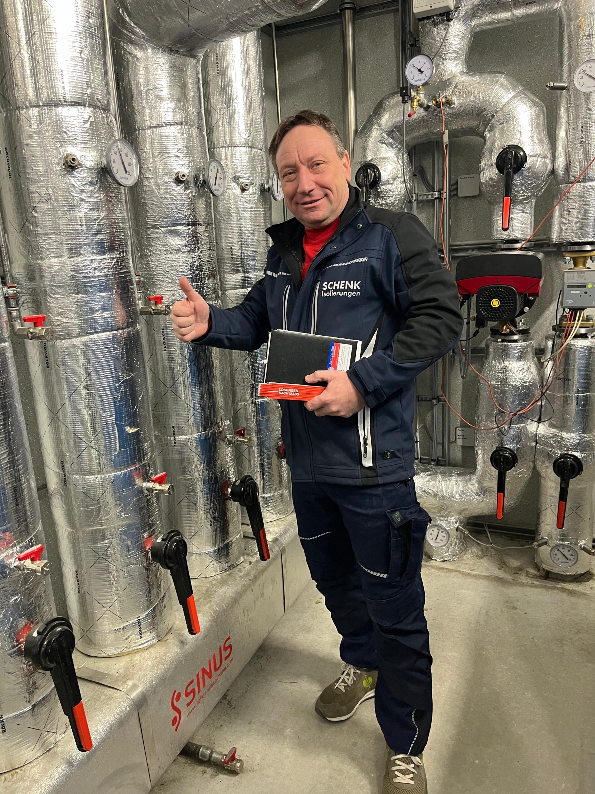 Andreas Schenk in Arbeitskleidung vor einer isolierten Heizungsanlage